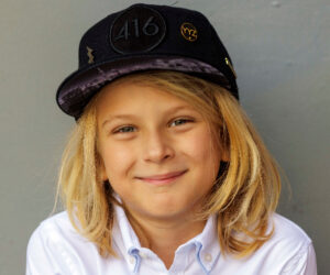 Max Keys's portait - he has brown eyes and shoulder-length blonde hair. He is wearing a white shirt and a fitted hat. 