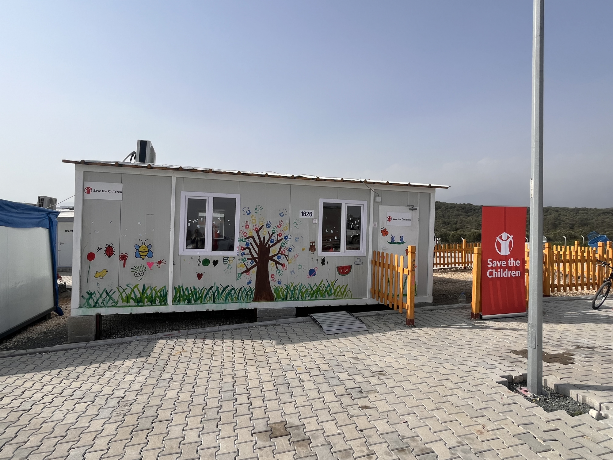 A classroom built from a shipping container with a mural painted along one side sits in an open area.